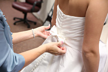 Mother helps her daughter into her wedding dress.