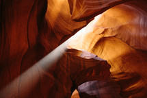 rays of sunlight shining into a red rock cave 