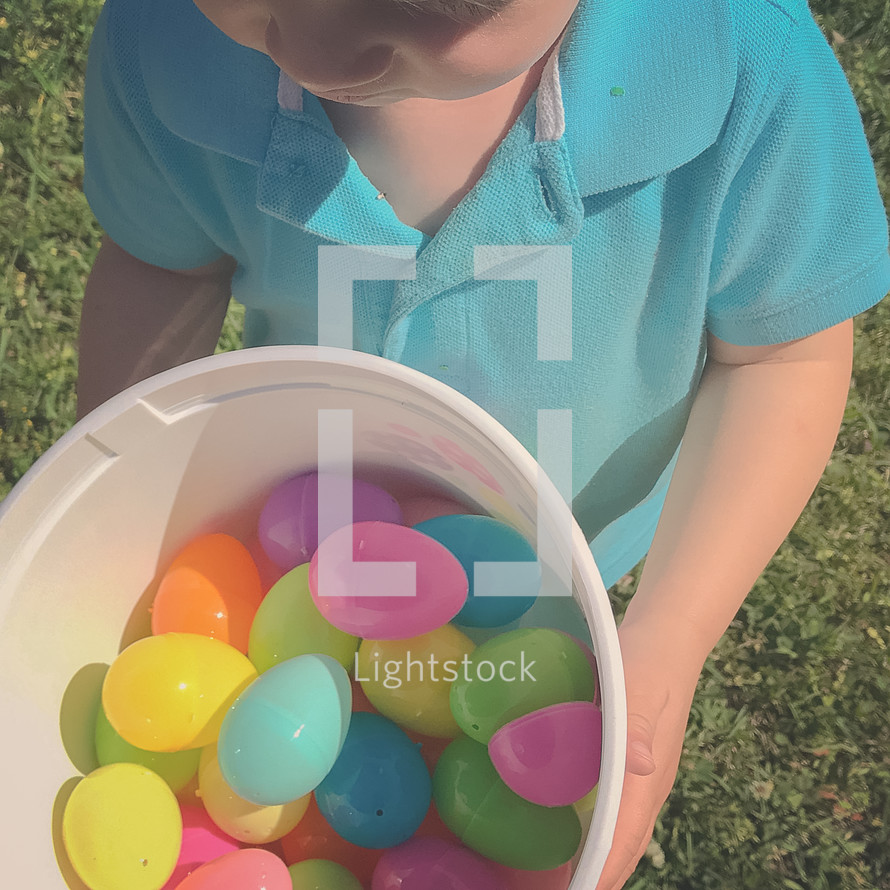 toddler boy holding a bucket of Easter eggs 