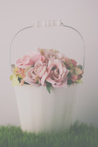 pink roses in a white pail on grass