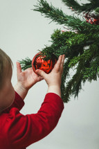 toddler playing with a Christmas ornament on a tree