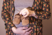 pregnant mother holding infant shoes 