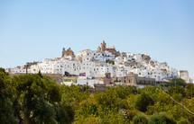 panoramic view of the white and old city of Ostuni on a hilltop and with the cathedral on top.