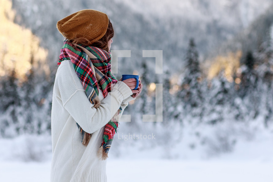 a woman standing in snow holding a warm mug 