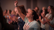 a woman at a worship service with hand raised 