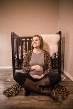 pregnant woman sitting on the floor of a nursery holding her belly 