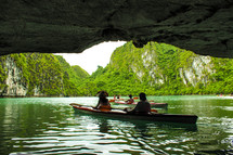 people in canoes exiting a sea cave 