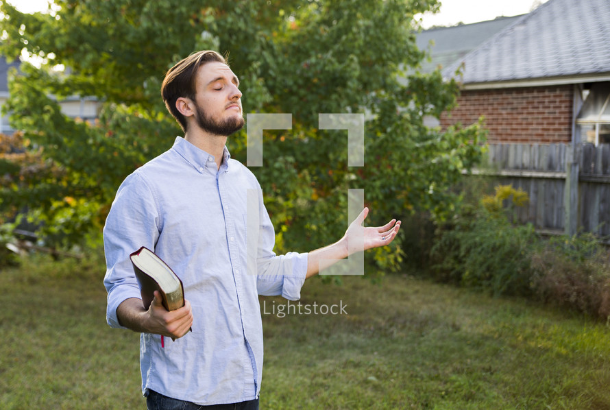 a man holding a Bible with arms raised 