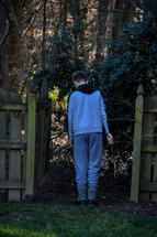 teen boy with a stick walking out a gate into a forest 