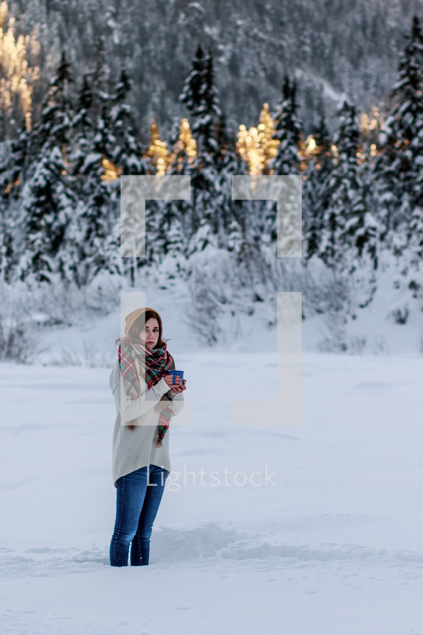 a woman standing in snow holding a warm mug 