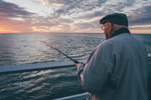 An older man fishes from a pier at sunset