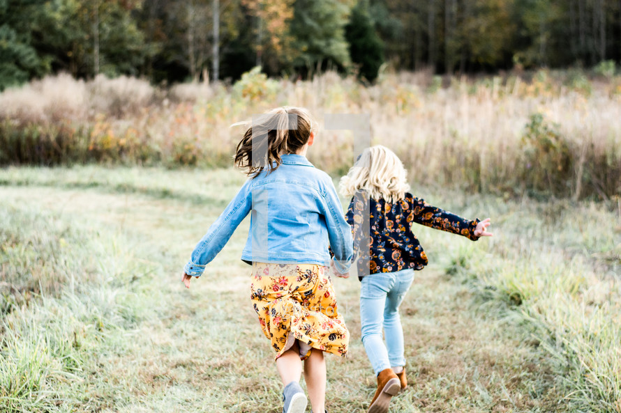 sisters walking through a field holding hands 