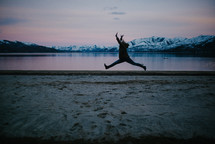 a woman leaping by a lake surround by snow capped mountains 