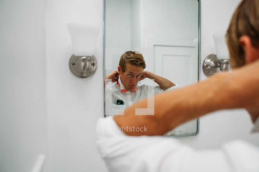 A man putting on a bowtie in a mirror 