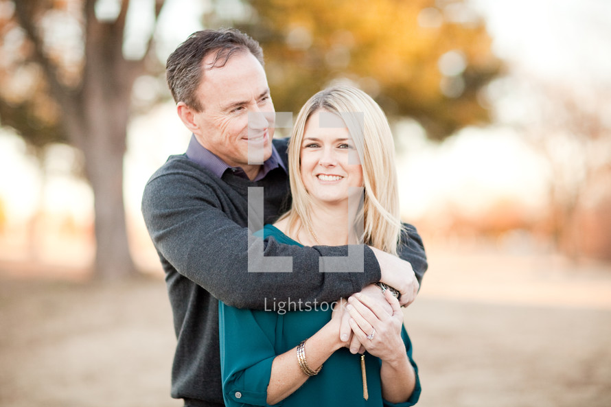 A husband hugging his wife in a field in the fall