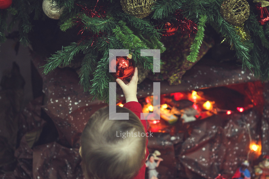 toddler playing with an ornament on a tree