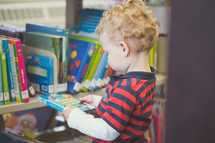 a toddler boy picking out books at the library 