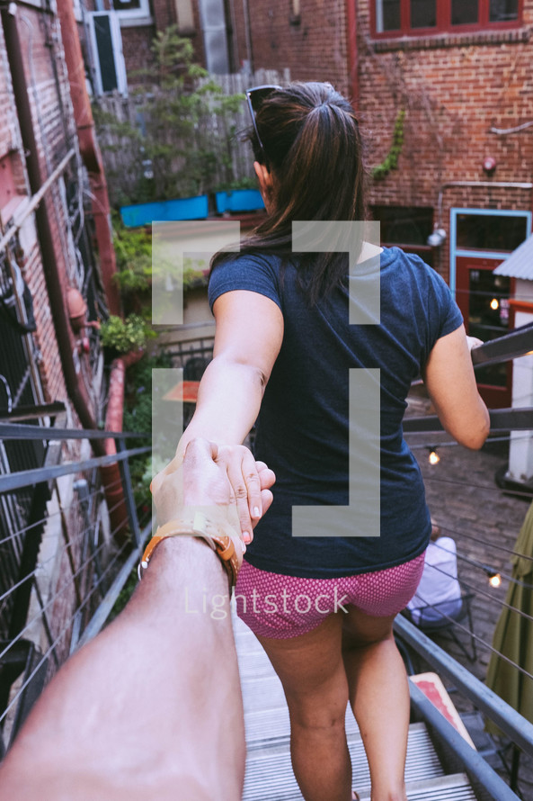 A young woman walking down steps while holding the hand of a young man.