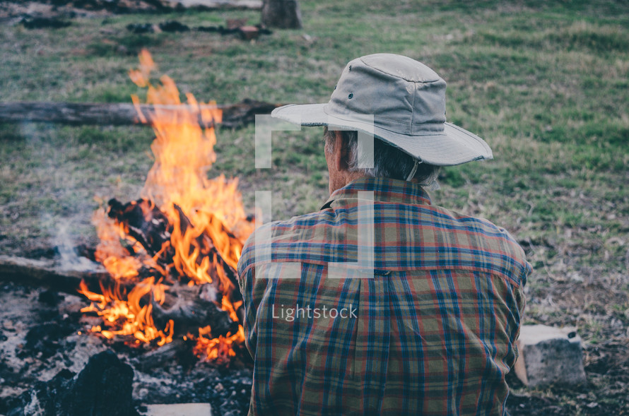 A man sit next to a camp fire.