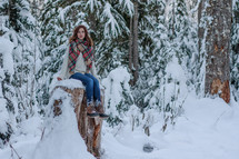 a woman sitting on a tree stump outdoors in snow 