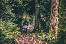 girl with a backpack walking into the woods 