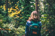 a girl with a backpack walking into the woods 