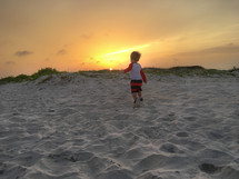a little boy running in the sand on a beach 