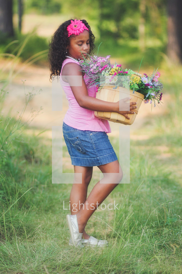 a girl carrying a basket of flowers down a dirt road 