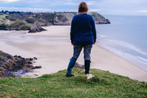 a woman in boots standing on a shore 