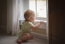 infant in a onesie looking out a window 
