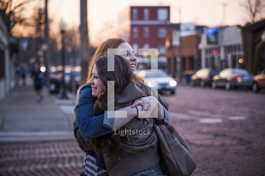 female friends hugging on a sidewalk 