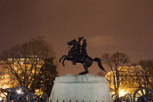 Bronze statue of Andrew Jackson on a horse, surrounded by cannons at night.