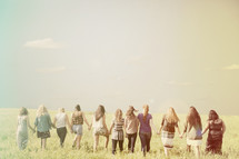 Teen girls holding hands, standing in a field.