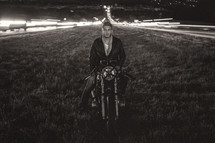 Man on a motorcycle in the grass, surrounded by busy highways at night.
