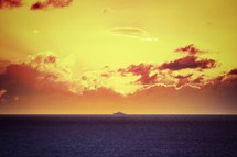 distant ship on the water under a yellow sky at sunset