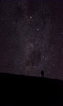 silhouette of a man standing on a mountaintop under stars in the night sky 