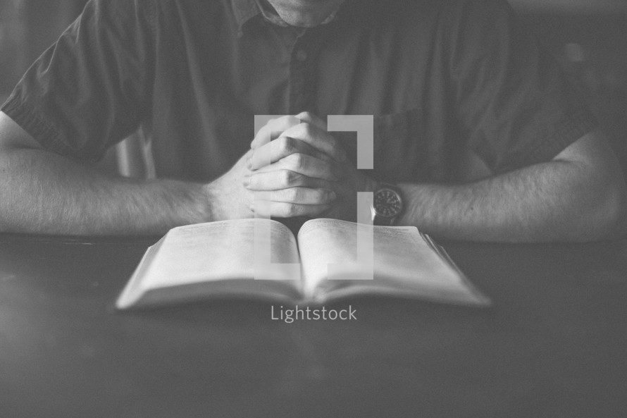 A man with hand folded in prayer in front of an open Bible