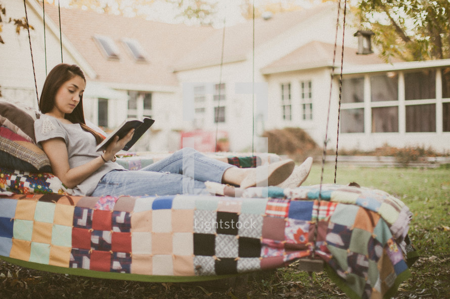 A young woman sitting on a swing and reading the Bible