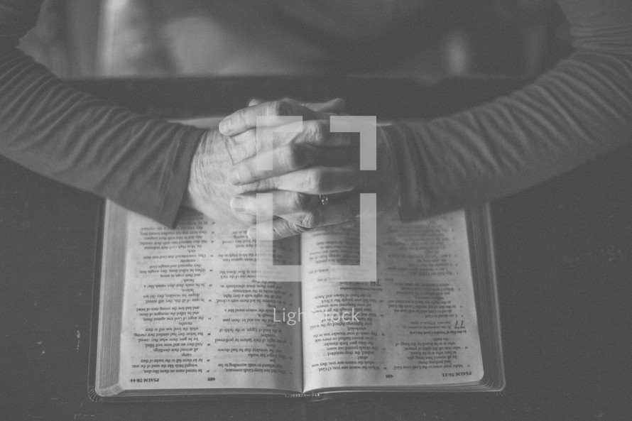 A woman's hands folded in prayer over an open Bible