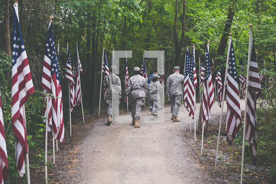 soldiers marching on a trail lined with American flags 