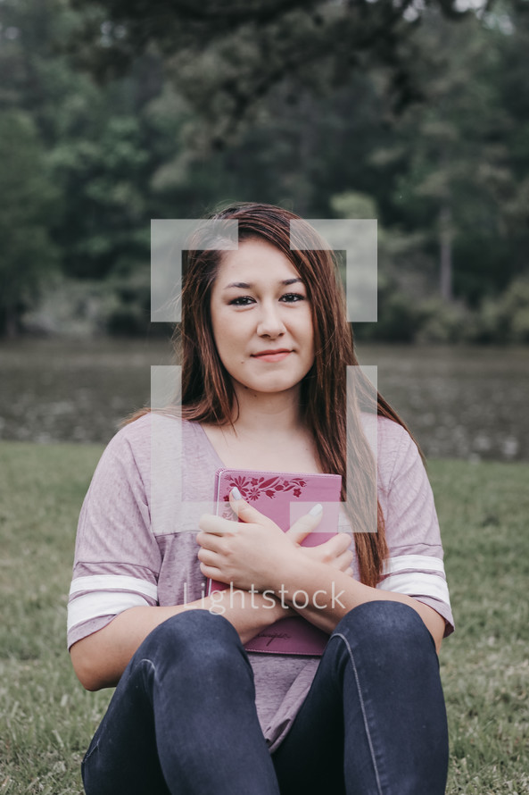 a young woman holding a Bible sitting in grass