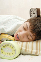 sleepy child next to three alarm clocks 
