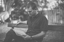 A young man sitting on a bench reading the Bible