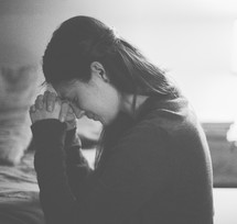 A woman kneeling in prayer beside her bed 