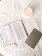 open Bible, wedding ring, journal, and candle on a tablecloth 