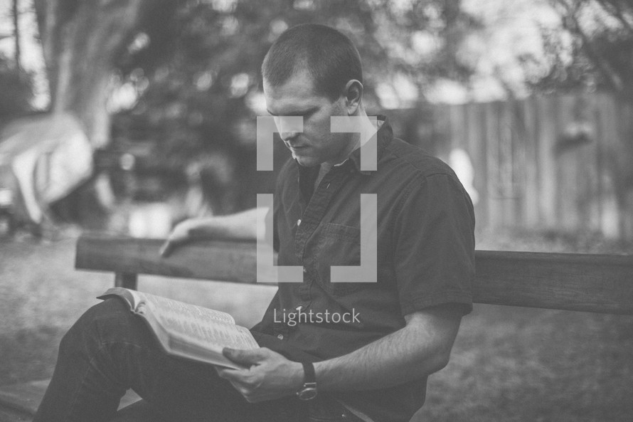 A young man sitting on a bench reading the Bible