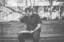 A young man sitting on a bench reading a Bible