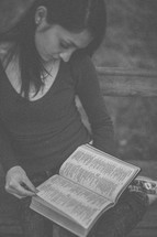 A young woman sitting on a bench reading a Bible