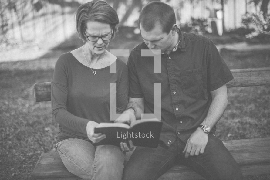 A man and woman sitting on a bench reading the Bible