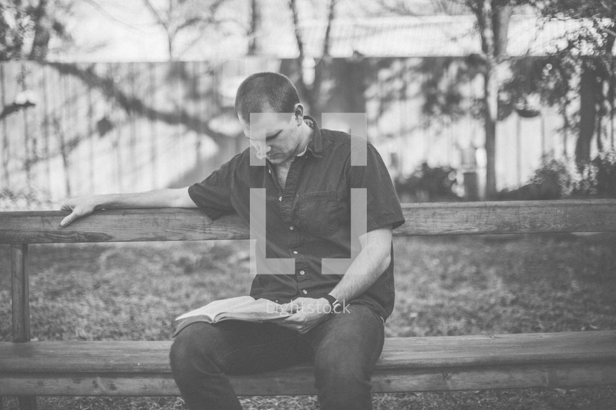 A young man sitting on a bench reading a Bible